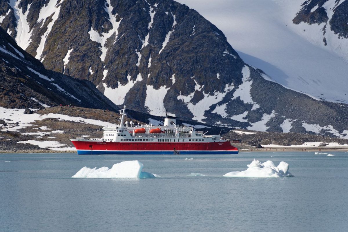 A red cruise ship sails through icy waters with snow-covered mountains in the background.